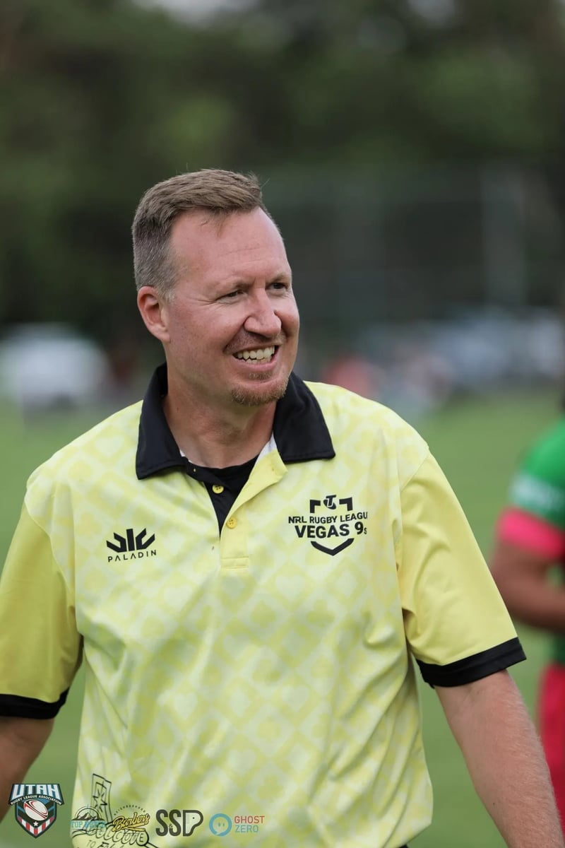 Referee in a yellow officiating polo smiles broadly on the field