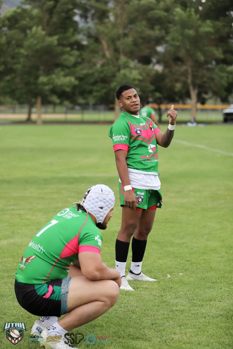 Rabbitahz player in green and red sharing a light moment with a seated teammate in a white scrum cap on the sideline