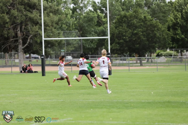 Players chase a breaking run into open field past the goalpost with spectators lining the far fence at the preseason double-header.