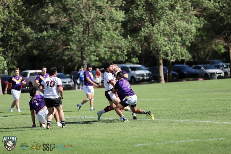 A Lehi Raiders ballcarrier in purple and gold is met head-on by Riverton Seagulls defenders in white and maroon.