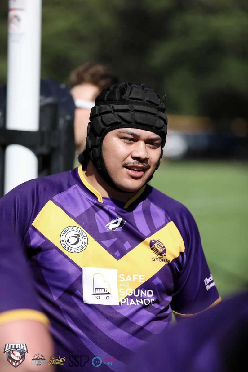 Smiling front-rower in a black scrum cap and purple-and-gold jersey between plays