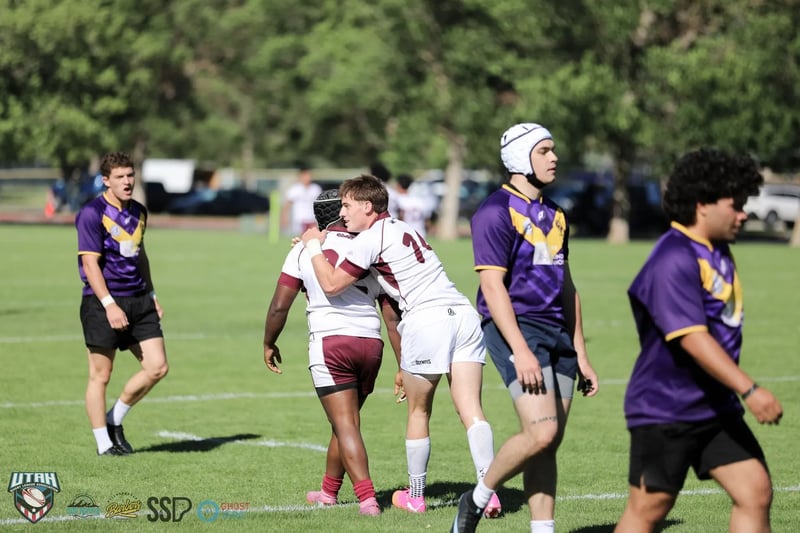 A Raiders player in purple and gold embraces a Seagulls opponent in white and maroon among teammates after the match.