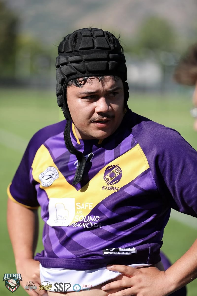 Raiders player in black headgear and a purple and gold jersey looks ahead with a focused expression between plays.