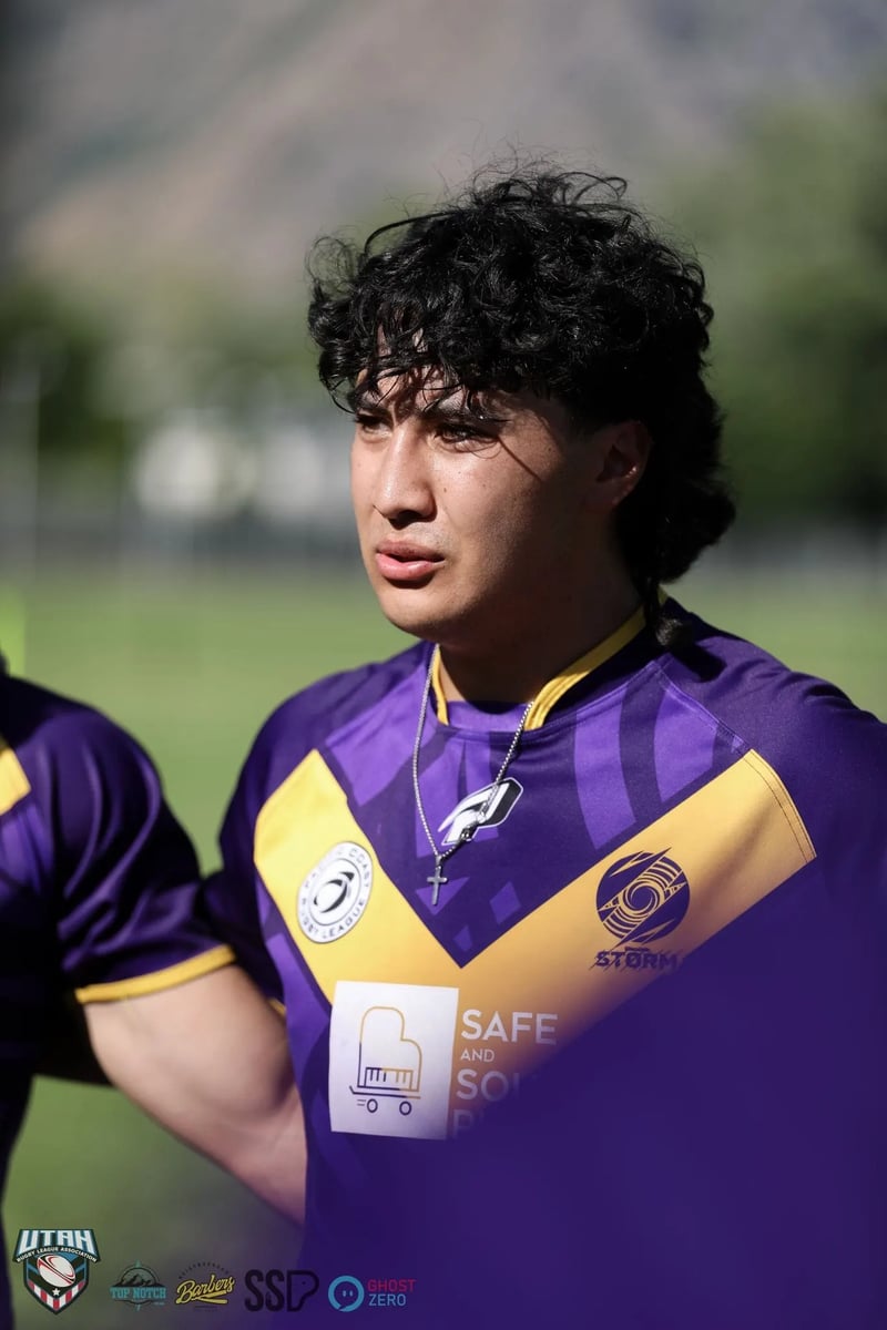 Young player in a purple and gold jersey looks up mid-huddle, face sweaty in warm evening light.