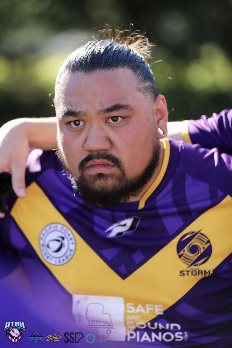 Broad-shouldered forward in a purple and gold jersey stares ahead with arms draped over teammates in the huddle.