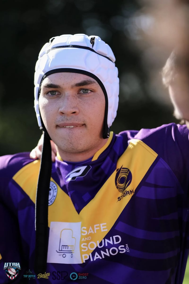 Player in a white scrum cap and purple and gold jersey looks straight into the camera from inside the team huddle.