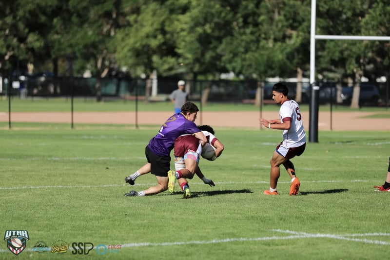 A Riverton Seagulls ballcarrier in maroon drives through a low Lehi Raiders tackle in open field.