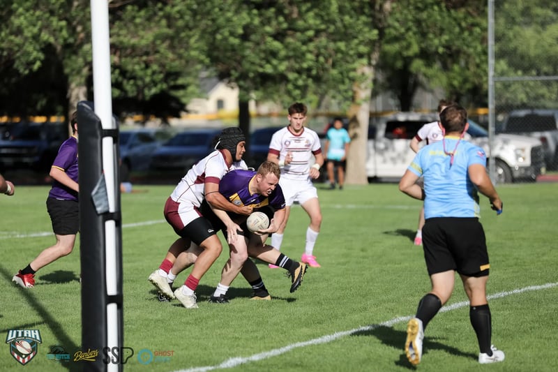 A Lehi Raiders ballcarrier in purple is wrapped up by Riverton Seagulls defenders near the goalpost pad.