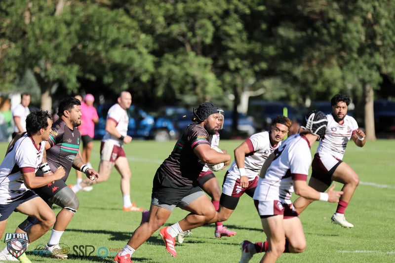 A Bluffdale Rabbitahz forward in a dark jersey charges into the Riverton Seagulls defence in white and maroon.
