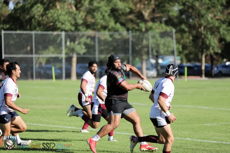 Rabbitahz ball-carrier in black with green and red hoops strides between two Seagulls defenders in white and maroon in open field.