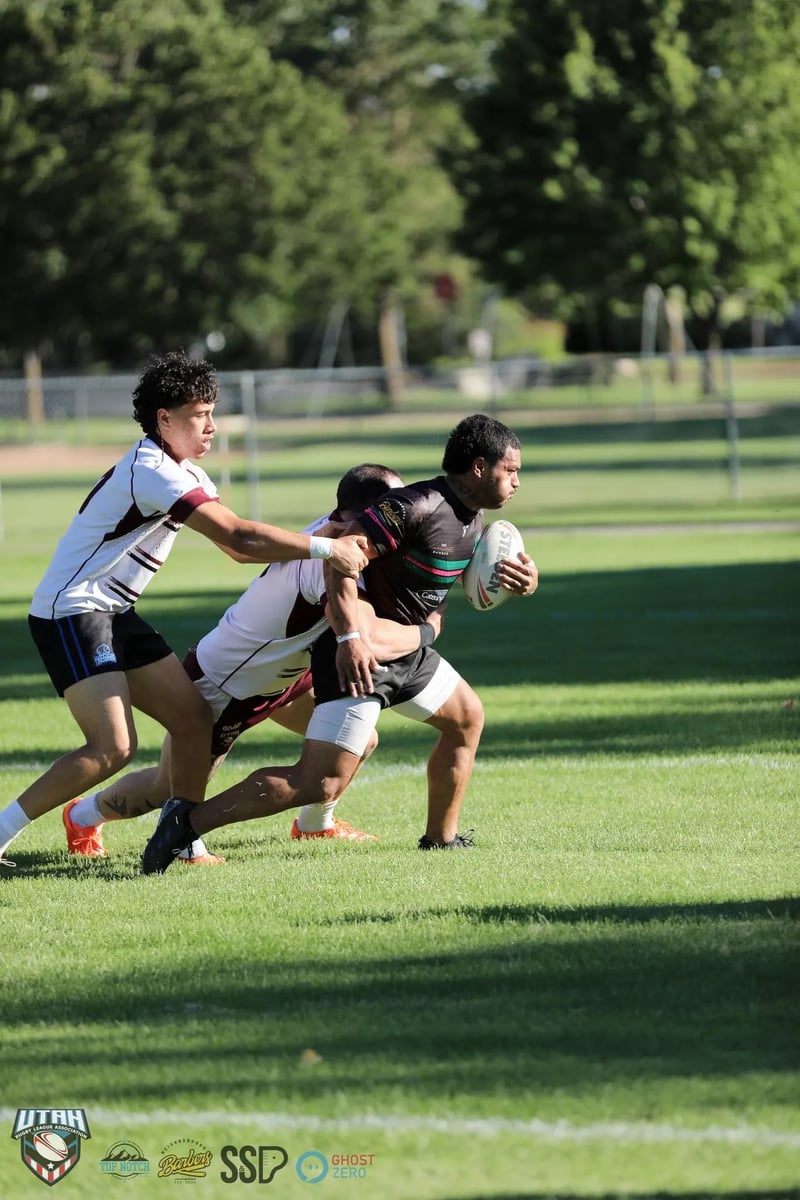 Rabbitahz ball-carrier in black drives forward with the ball clamped in one arm as two white-shirted Seagulls tacklers hang off him.