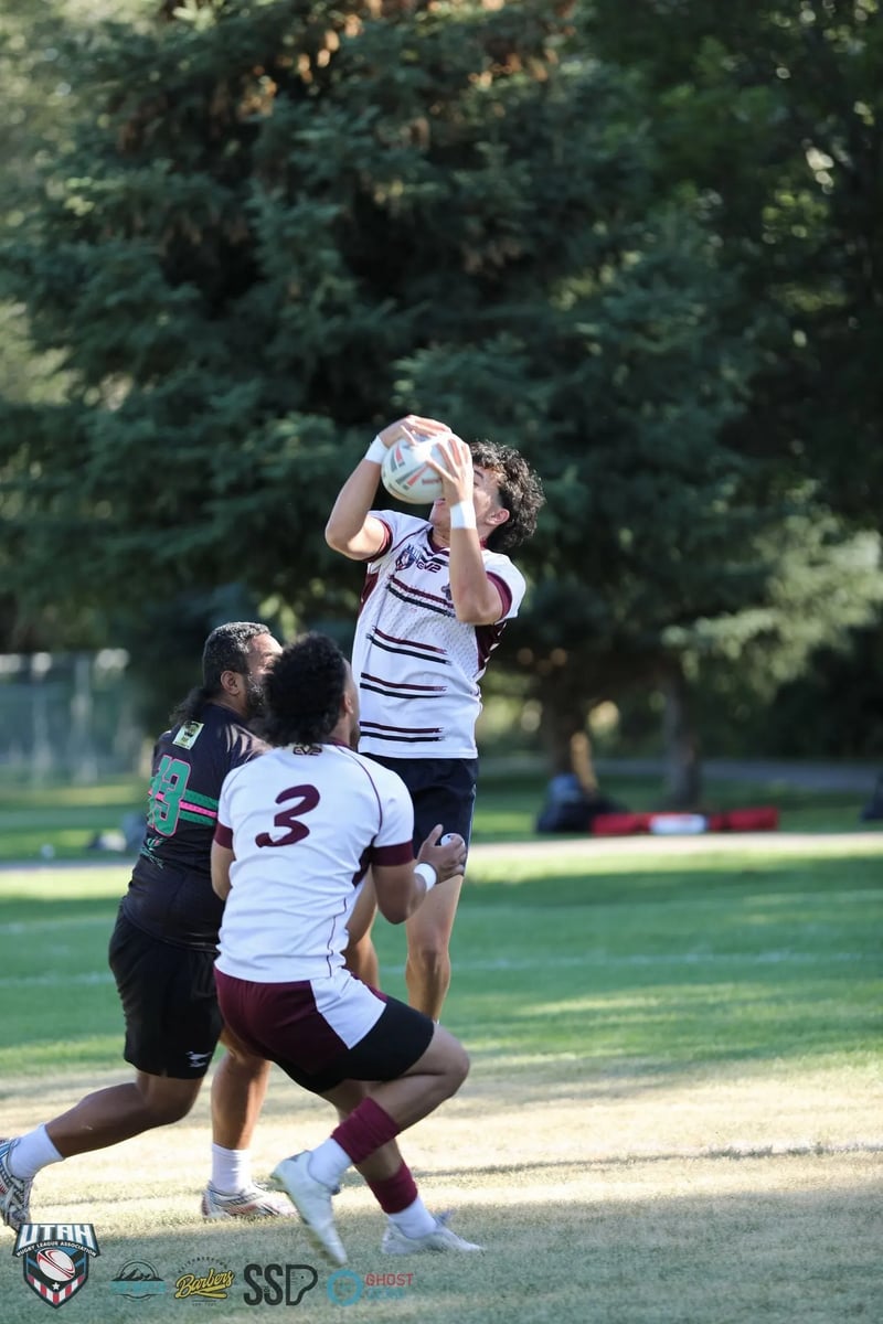 Riverton Seagulls player in white and maroon leaps high above two opponents to claim a clean overhead catch with both hands.