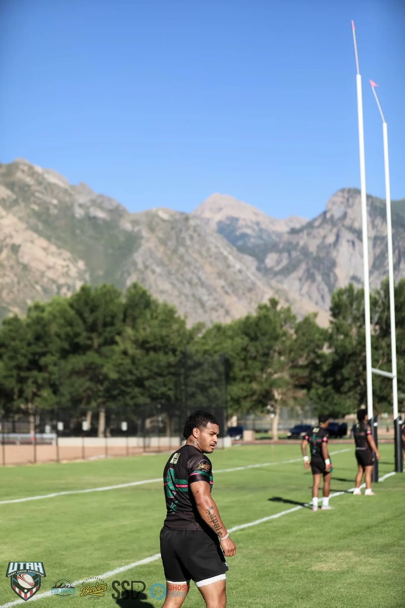 Rugby goalposts and a tree line with the rocky Wasatch mountains rising behind the field in late-afternoon light.