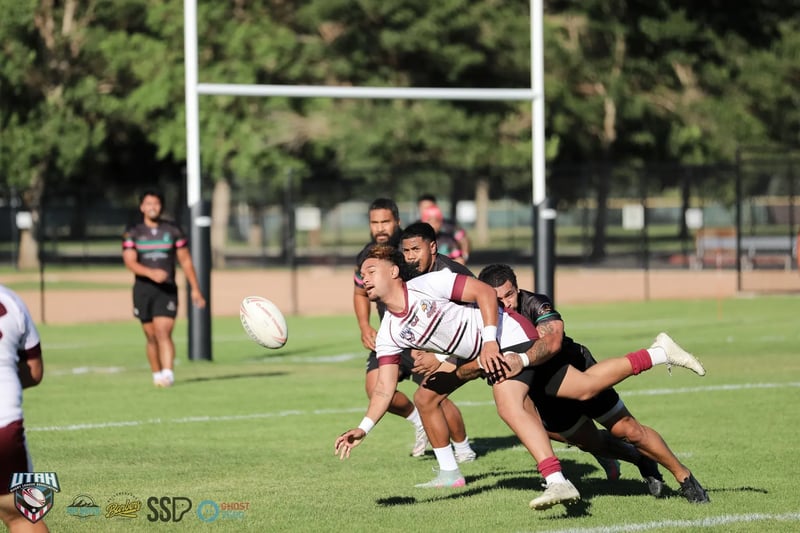 Seagulls player in white and maroon flings a pass as he is dragged down by a Rabbitahz defender, the ball frozen in mid-air near the posts.
