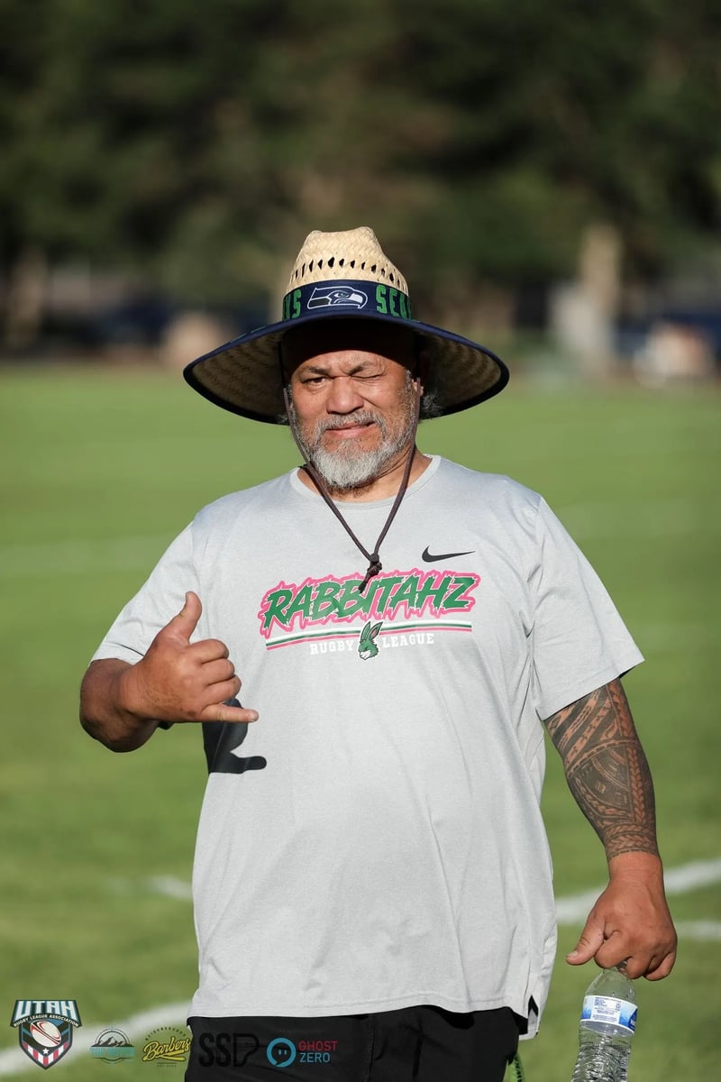 A Rabbitahz supporter in a wide-brimmed straw hat and white Rabbitahz t-shirt throws a shaka to the camera on the sideline.