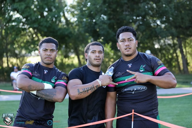 Three Rabbitahz players in black jerseys with green and pink trim pose together behind the sideline rope, the middle player crossing his arms.