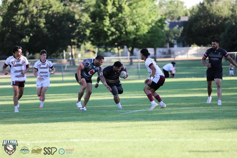 A Rabbitahz ball carrier in a black jersey steps between two Seagulls defenders in white and maroon in open midfield.
