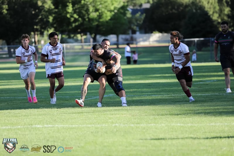 Head-on tackle in midfield: a Seagulls defender in white and maroon wraps up a Rabbitahz ball carrier in black as players from both teams converge.