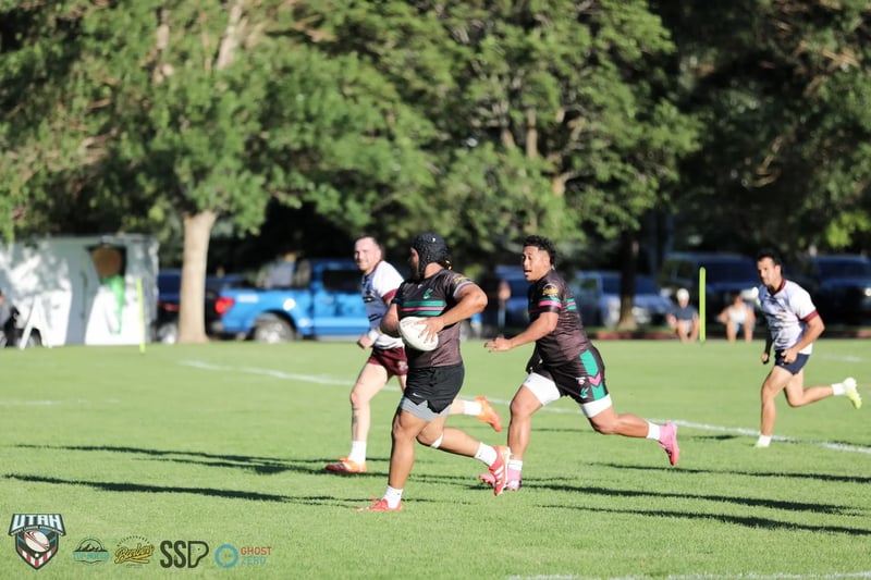 A Rabbitahz ball carrier in black headgear breaks into open field with the ball tucked under one arm, a Rabbitahz teammate and Seagulls chasers in white and maroon in pursuit.