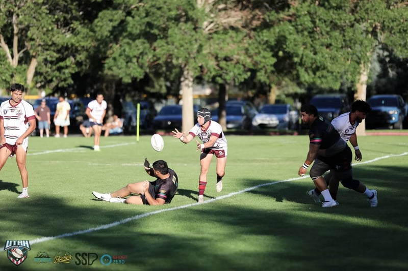 A Rabbitahz player seated on the turf flicks the ball away after a tackle, the ball frozen mid-air in front of an onrushing Seagulls defender in white and maroon.