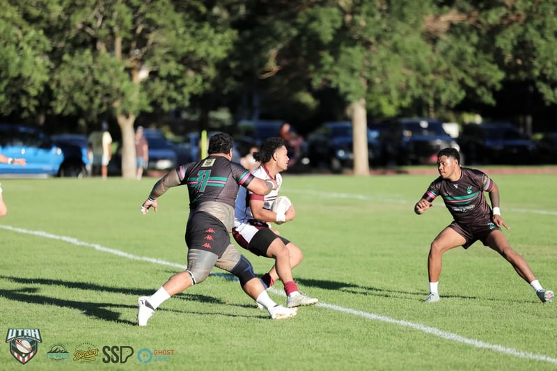 Wide open-field frame of a Rabbitahz ball carrier in dark kit angling away as a lone defender stretches to close him down on the sunlit pitch.