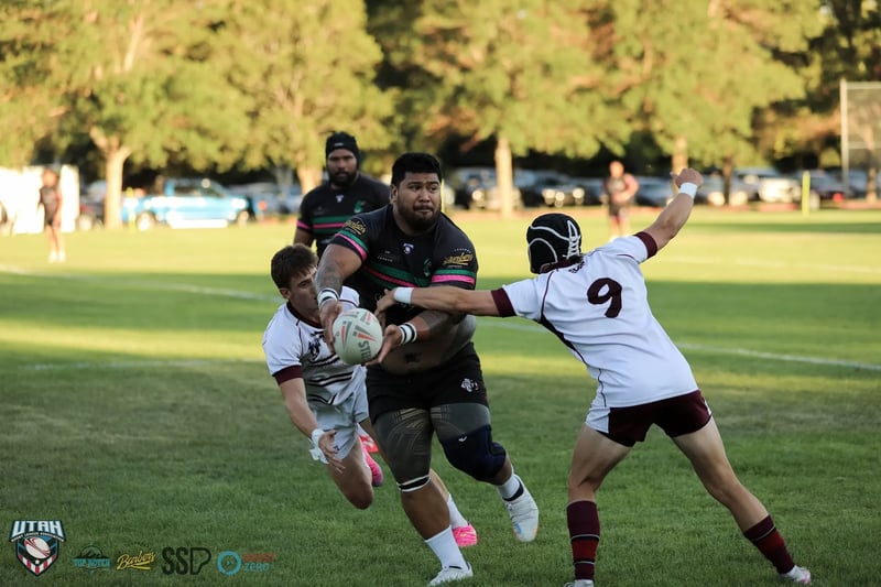 A Rabbitahz ball carrier in dark kit fends off a diving Seagulls number 9 in white and maroon, holding the ball away in one hand.