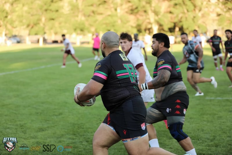 A big Rabbitahz forward in dark green-and-red-trimmed kit charges upfield ball in hand with a Seagulls defender in white moving to meet him.