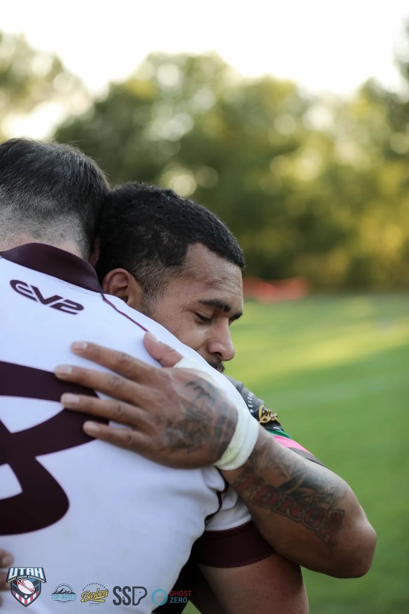 Two opponents share a close embrace after full time, one in the Seagulls' white jersey resting his head on the other's shoulder.
