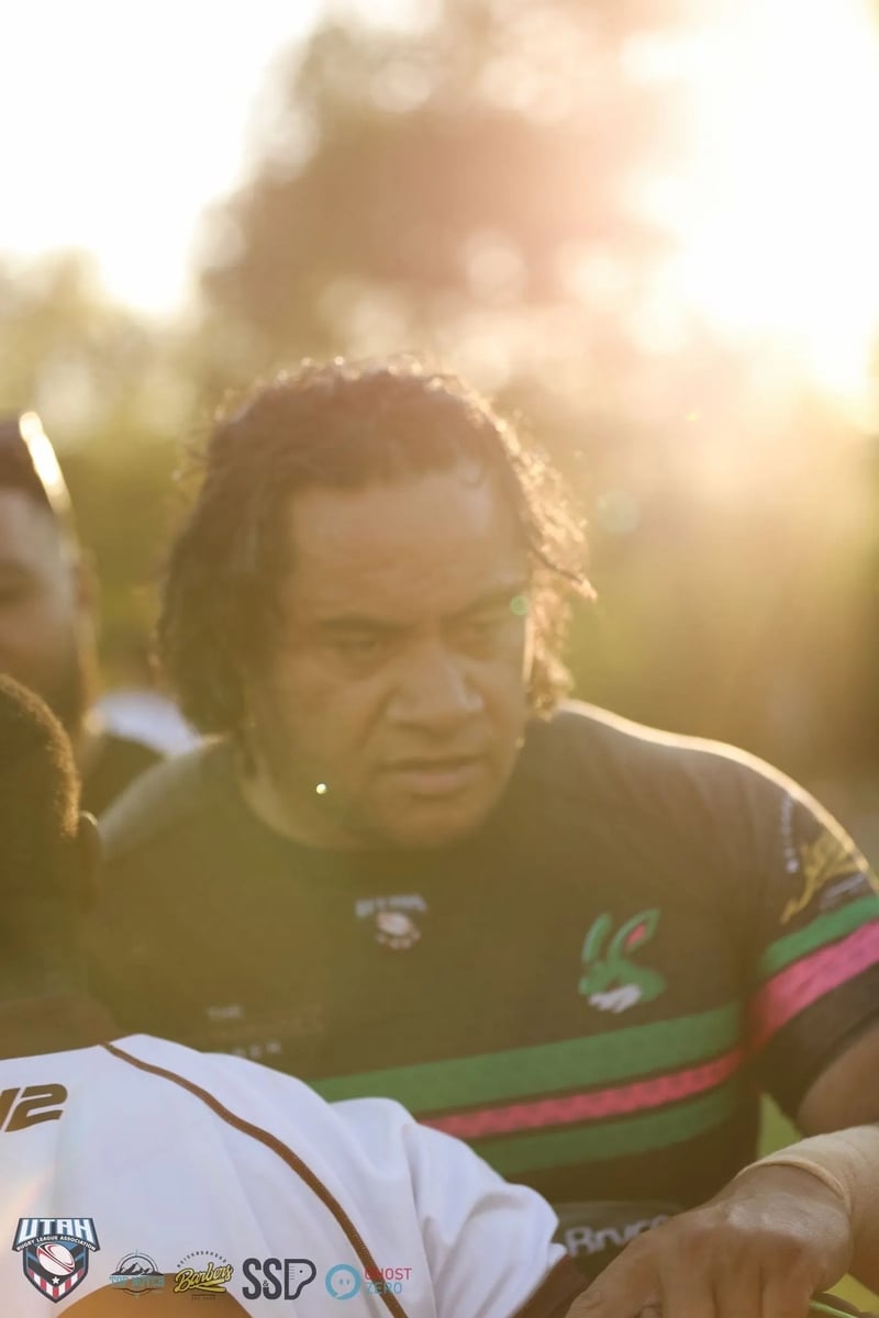 A long-haired man in a dark jersey lit by dramatic golden backlight and lens flare during the post-match gathering.