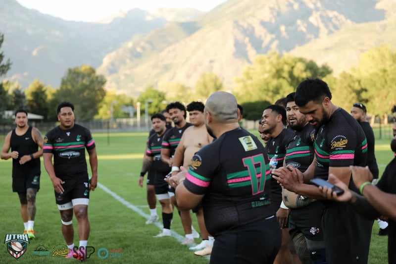 Rabbitahz players in dark kits with green and red trim line up across the field for post-match handshakes with the Wasatch mountains glowing behind them.