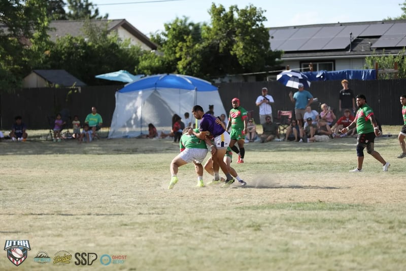 A tackle throws up dust midfield in front of large blue and white canopy tents and rows of festival spectators lining the fence at the Samoan festival grounds.