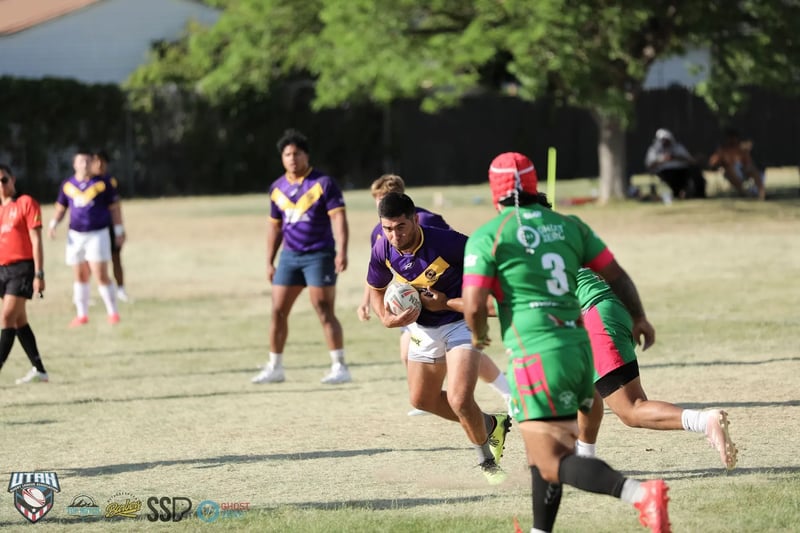 Raiders ball carrier in purple and gold cuts sharply off his left foot as a Rabbitahz defender in green with a red scrum cap gives chase in the foreground.