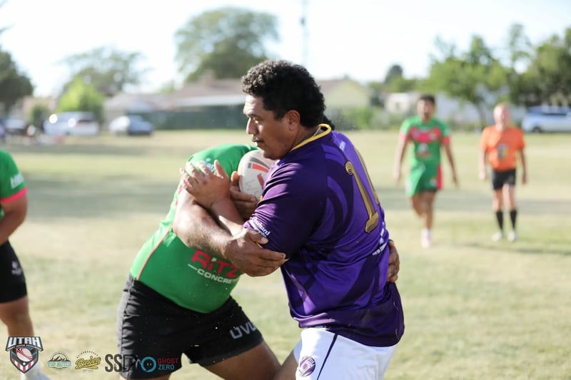 A Raiders forward in purple drives the ball into a wrapping tackle from a Rabbitahz defender in green, the two locked chest to chest at close quarters with a touch judge in orange behind.