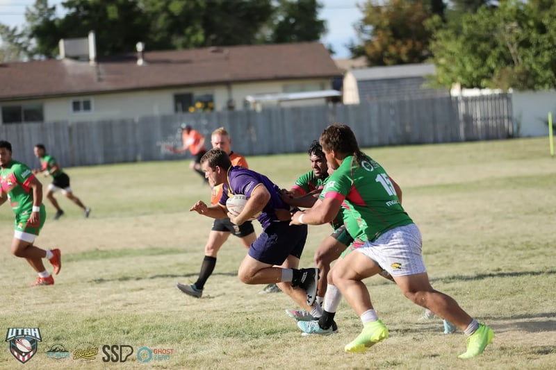 Raiders ball carrier in purple bursts through a gap between two lunging Rabbitahz defenders in green and red.