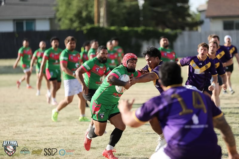 Rabbitahz ball carrier in a red headguard is wrapped up by a Raiders defender in purple number 14 as green support arrives