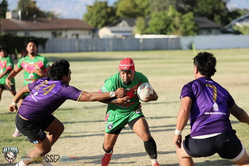 A Rabbitahz ball-carrier in green wearing a red scrum cap fends off a lunging Raiders defender in purple in midfield.