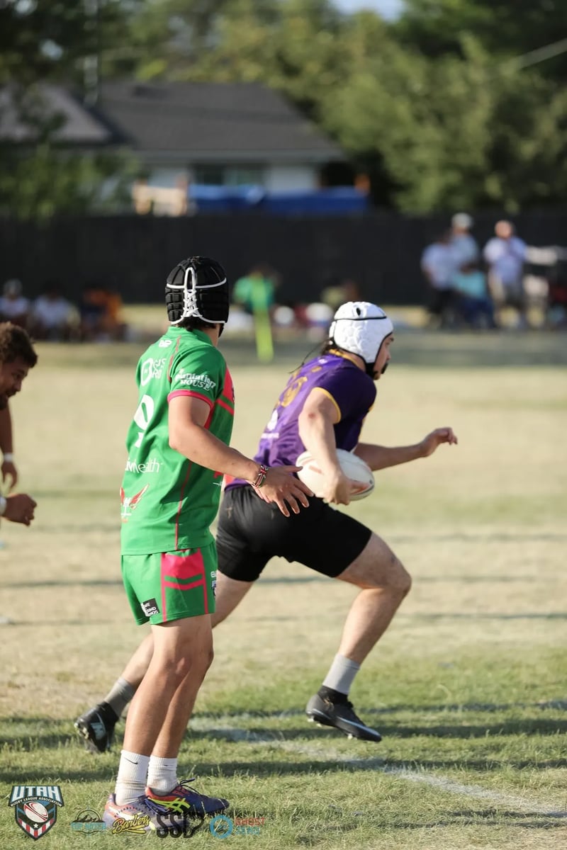A Rabbitahz defender in green closes in and grabs at a Raiders ball-carrier in purple with a white scrum cap as he tries to break away.