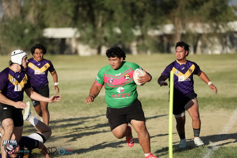 A big Rabbitahz forward in green and red carries the ball straight ahead past a yellow corner post, Raiders defenders in purple and gold trailing behind.