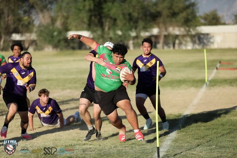 A powerful Rabbitahz forward in green and red throws a high fend as Raiders defenders in purple and gold drape off him in golden-hour light.
