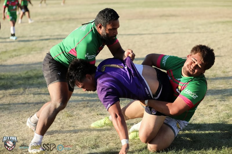A Rabbitahz defender in green hauls a Raiders ball-carrier in purple down to the ground in a wrestling tackle.