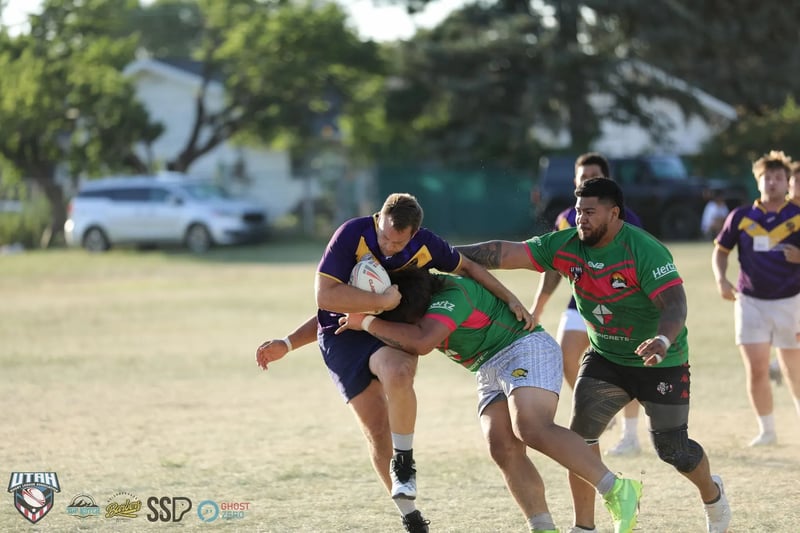 A Rabbitahz defender in green and red drives into a Raiders ball-carrier in purple and gold, the ball clamped between them.