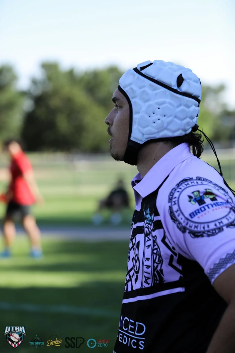 A Lehi Raiders player in white headgear watches the play from the touchline.