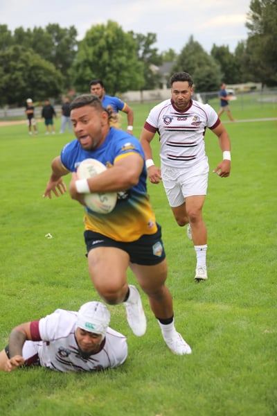 Broncos ball carrier breaking away from a diving defender in white and maroon
