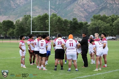 Provo Broncos players huddle near the goalposts with the Wasatch mountains rising behind the field