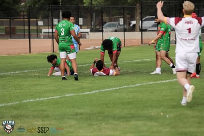 Broncos player raises both arms after a try while Rabbitahz defenders kneel on the turf