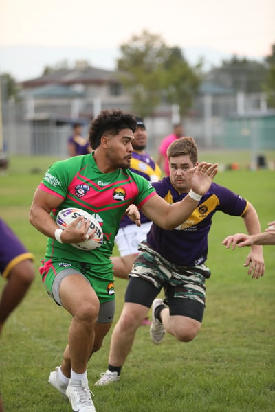 Rabbitahz ball carrier in green and pink fending off a Raiders defender in purple and gold