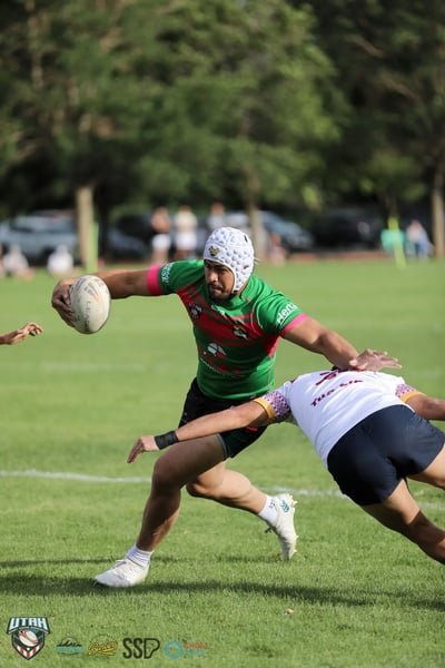 Rabbitahz ball carrier in green and red with white headgear palms off a diving Broncos tackler during the preseason Hopoate Cup match