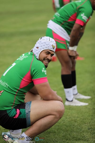 Smiling Rabbitahz player in a white scrum cap shares a laugh while kneeling on the sideline