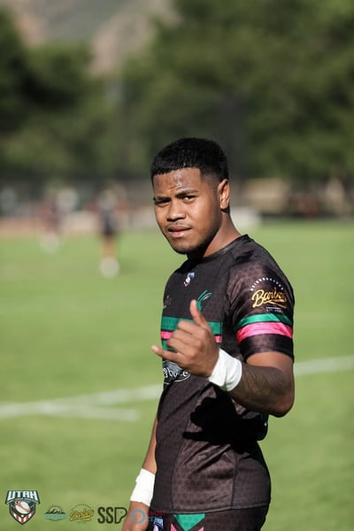 Bluffdale Rabbitahz player in a black jersey with green and red hoops looks back at the camera and flashes a shaka sign in golden evening light.