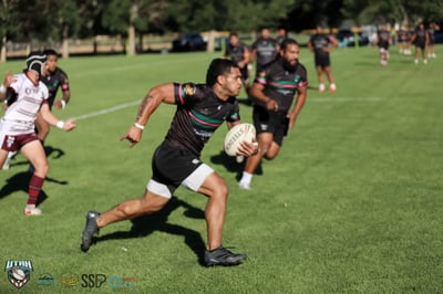 Rabbitahz player in black with green and red hoops sprints upfield with the ball tucked under his arm, defenders trailing behind.